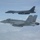 170214-N-XZ522-005 Two U.S. military aircraft are flying in formation above a cloud layer. The foreground aircraft is a U.S. Navy F/A-18 Super Hornet bearing tail code 'NE' and modex '303', while the background aircraft is a U.S. Air Force B-1B Lancer strategic bomber with tail code 'DY'. This appears to be a joint service formation flight, likely a training or escort mission.