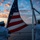 170211-N-BL637-050 Two U.S. Navy sailors in dress white uniforms are raising or lowering the American flag on the stern of a naval vessel at either sunrise or sunset. The scene is set over open water with a dramatic sky featuring orange, pink, and blue clouds. The composition is a silhouette-style photograph emphasizing the ceremonial nature of the flag detail.