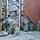 170213-N-N0901-006 A soldier in multicam/OCP camouflage uniform is crouched on a gravel surface, working with what appears to be demolition or breaching equipment including a wooden board, detonation cord (det cord), and a black initiating device. The setting appears to be a military training environment with plywood walls, sandbags, and large rocks visible in the background. The activity is consistent with combat engineering or explosive ordnance training.