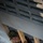 Nations make progress on multipurpose room A person wearing camouflage military uniform and cap is looking upward through a narrow gap between concrete structural elements, smiling at the camera. The individual appears to be working in a construction or engineering context, holding a wooden support beam. The photo is taken from above, looking down at the subject.