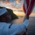 170211-N-BL637-025 A U.S. Navy sailor in dress whites is raising or handling an American flag at sunrise or sunset, with a coastal landscape and ocean visible in the background. The sailor wears a white Dixie cup cover and glasses, and a ship name tag is visible on the uniform. The image is a dramatic, professionally composed military photograph with warm golden-hour lighting.