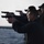 170215-N-JI086-139 A group of individuals are participating in a firearms training or qualification exercise at what appears to be an outdoor shooting range. Multiple shooters are lined up in a row, each aiming semi-automatic pistols in the same direction. The foreground shooter is wearing protective eyewear and ear protection, suggesting a formal or supervised training environment.