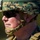 10th Marine Regiment HIMARS Firing Excercise A close-up photograph of a military personnel wearing MARPAT (Marine Pattern) digital camouflage helmet and uniform, consistent with U.S. Marine Corps equipment. The subject is equipped with tactical ballistic sunglasses labeled 'APEL' and a tan/coyote colored chin strap with quick-release buckles. A device, possibly a camera or sensor mount, is visible attached to the front-left of the helmet.