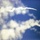 10th Marine Regiment HIMARS Firing Excercise The image shows what appears to be one or two rocket or missile contrails arcing across a blue sky with scattered white clouds. A bright point of light is visible at the leading edge of the upper contrail, suggesting an active propulsion source. The image is slightly out of focus, making precise identification of the object difficult.