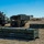 10th Marine Regiment HIMARS Firing Excercise The image shows military personnel operating what appears to be an M270 Multiple Launch Rocket System (MLRS) or similar rocket artillery system mounted on a heavy tactical vehicle. Several soldiers are working around the launcher in an open field environment. Multiple ammunition transport containers with rocket pods are staged on the ground nearby, suggesting a loading or reloading operation.