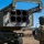 10th Marine Regiment HIMARS Firing Excercise A military service member in camouflage uniform and tactical gear stands beside a Multiple Launch Rocket System (MLRS) mounted on a military vehicle. The launcher pod shows six empty rocket tubes, indicating rounds have been fired or the pod is being inspected. The setting appears to be an open training range or field exercise under clear blue skies.