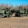 10th Marine Regiment HIMARS Firing Excercise The image shows two military multiple launch rocket systems (MLRS), specifically appearing to be M142 HIMARS or M270 MLRS variants, positioned in an open field with bare winter trees in the background. Two military personnel in camouflage uniforms are visible, one climbing on the left vehicle and one standing near the right vehicle. The vehicles are painted in standard olive drab/military green and appear to be in an operational or training configuration.