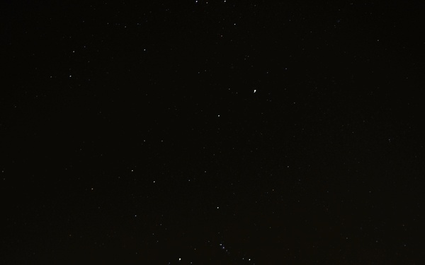 A night photograph of a military jet aircraft, specifically showing the forward fuselage and cockpit canopy illuminated by artificial lighting against a dark starry sky. The aircraft bears the tail number 335 and standard military markings including a 'RESCUE' label with an arrow indicator near the cockpit. The long-exposure shot captures multiple stars visible in the night sky above the aircraft.