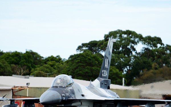 A U.S. Air Force F-16 Fighting Falcon fighter jet is taxiing on a runway apron at what appears to be a military airfield. The aircraft bears the tail code 'AK' indicating it belongs to the Alaska Air National Guard, with serial number 96-304 visible on the tail. The jet is armed with air-to-air missiles on its wingtips and carries additional ordnance under its wings.