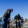 Arbor Day "Adopt an Island" Three workers are engaged in ground-breaking or demolition work in what appears to be a parking lot or landscaped median area. Two individuals are operating DeWalt electric jackhammers/demolition hammers to break up compacted soil or concrete, while a third person assists with a shovel. Additional workers are visible in the background performing similar tasks.