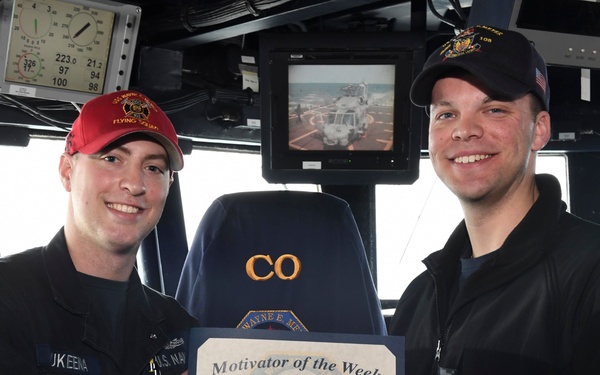 Two U.S. Navy personnel are posing on the bridge of a naval vessel, holding a 'Motivator of the Week' certificate awarded to HTFN (SW) Shawn Sukeena for the week of March 18-24, 2017. The ceremony appears to take place aboard DDG-108, with the Commanding Officer's chair visible in the background. Both individuals are smiling and shaking hands while presenting the award.