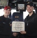 Two U.S. Navy personnel are posing on the bridge of a naval vessel, holding a 'Motivator of the Week' certificate awarded to HTFN (SW) Shawn Sukeena for the week of March 18-24, 2017. The ceremony appears to take place aboard DDG-108, with the Commanding Officer's chair visible in the background. Both individuals are smiling and shaking hands while presenting the award.