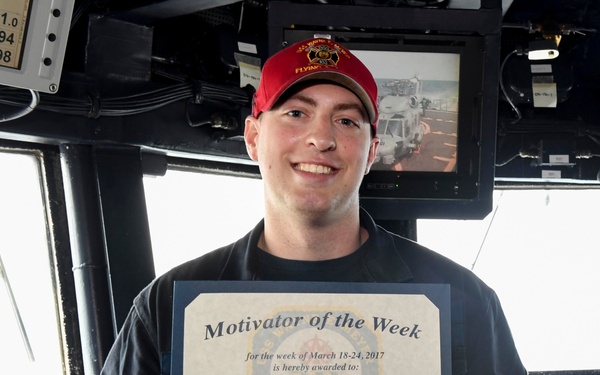 A smiling young sailor aboard USS Wayne E. Meyer (DDG 108) holds a 'Motivator of the Week' certificate awarded for the week of March 18-24, 2017. The certificate is awarded to HTFN (SW) Shawn Sukeena and is signed by Commanding Officer Vincent A. Forston, CDR. The photo appears to be taken on the ship's bridge, surrounded by navigation equipment and monitors.