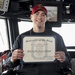 A smiling young sailor aboard USS Wayne E. Meyer (DDG 108) holds a 'Motivator of the Week' certificate awarded for the week of March 18-24, 2017. The certificate is awarded to HTFN (SW) Shawn Sukeena and is signed by Commanding Officer Vincent A. Forston, CDR. The photo appears to be taken on the ship's bridge, surrounded by navigation equipment and monitors.