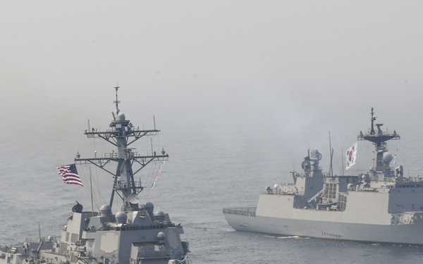 Two military warships are sailing in formation on open ocean waters under hazy atmospheric conditions. The foreground vessel is a US Navy Arleigh Burke-class guided-missile destroyer flying the American flag, bearing hull number 109. The background vessel is a Republic of Korea Navy destroyer flying the South Korean flag, indicating a joint naval exercise or patrol operation.