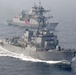 The image shows a formation of naval warships underway at sea, with a U.S. Navy Arleigh Burke-class guided-missile destroyer bearing hull number 108 in the foreground. Behind it are at least two additional warships, one of which displays a South Korean flag, suggesting a joint naval exercise or patrol operation. The ships are moving at speed, generating visible bow waves and wakes.