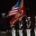 Marine Barracks Washington Evening Parade April 28, 2017 A United States Marine Corps color guard ceremony is being conducted at night, likely at Marine Barracks Washington or a similar formal military installation. Personnel in dress blues with white trousers and white covers are presenting the U.S. national flag and the Marine Corps flag. Additional Marines in formation are visible in the background.