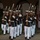 Marine Barracks Washington Evening Parade April 28, 2017 A precision drill team, identifiable as U.S. Marines based on their distinctive dress blue uniforms with red trim and white trousers, performs a ceremonial rifle drill at night. The Marines are marching in tight formation while carrying M1 Garand rifles with fixed bayonets at uniform angles. The event appears to be a formal evening parade or ceremonial performance, likely at a military installation.