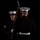 Marine Barracks Washington Evening Parade April 28, 2017 Two U.S. Marine Corps personnel in dress blues uniform are photographed against a black background, appearing to perform a ceremonial drill or inspection. The Marine facing the camera displays a Corporal rank chevron on his left sleeve and is holding a rifle at an angled position. The dramatic lighting and dark background suggest a formal ceremonial or portrait setting.