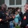 Marine Barracks Washington Evening Parade April 28, 2017 Two U.S. Marines in dress blue uniforms are engaged in conversation at what appears to be a military social event or ceremony. The senior Marine on the left displays a high-ranking enlisted insignia and numerous service medals, while the junior Marine on the right wears a lower enlisted rank insignia. Civilians, including families with children, are visible in the background near a shelving unit holding white dress covers.