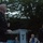 Marine Barracks Washington Evening Parade April 28, 2017 A U.S. Marine Corps officer in dress blues is speaking at a clear acrylic podium bearing what appears to be a military emblem with the year '1801'. The outdoor evening event appears to be a formal military ceremony or reception, with at least one other uniformed officer and civilian attendees visible in the background. The setting is an outdoor garden or courtyard surrounded by trees.