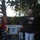 Marine Barracks Washington Evening Parade April 28, 2017 A U.S. Marine Corps officer in dress blues uniform stands at a clear podium speaking into a microphone at an outdoor evening ceremony. The podium displays what appears to be a U.S. Marine Corps emblem with the numbers '1801' visible. Musicians in red uniforms are visible in the background, suggesting a formal military ceremonial event.