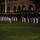Marine Barracks Washington Evening Parade April 28, 2017 A large formation of U.S. Marines in dress blue uniforms with white trousers are assembled in a ceremonial parade or evening parade formation. They are standing in precise rows on a manicured grass lawn in front of a red brick building with arched colonnades. The scene appears to be a formal military ceremony, likely an Evening Parade.