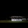 Marine Barracks Washington Evening Parade April 28, 2017 A nighttime military ceremonial drill is taking place on a grass field, illuminated by spotlights against a completely dark background. A formation of uniformed personnel, dressed in dark jackets and white trousers with white caps, are performing a rifle manual or precision drill exercise. The dramatic lighting isolates the formation, creating a stark visual contrast.