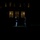 Marine Barracks Washington Evening Parade April 28, 2017 A nighttime ceremonial military scene showing two uniformed figures on a lawn in front of a large illuminated building. One figure appears to be performing a rifle drill or manual of arms, with the weapon raised vertically. The scene is dramatically lit with the building's warm window light providing the primary illumination.
