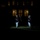 Marine Barracks Washington Evening Parade April 28, 2017 A nighttime military ceremony is taking place on a grass field in front of an illuminated building. A lone figure in dress uniform marches forward while tossing or catching a ceremonial baton, with a line of uniformed personnel standing at attention to the right. The scene is dramatically lit with spotlights against an otherwise dark environment.