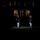 Marine Barracks Washington Evening Parade April 28, 2017 A nighttime military ceremony is taking place on a grass lawn in front of a large illuminated building. One Marine in dress uniform stands apart from a group of fellow Marines, all carrying rifles and wearing distinctive white caps and white trousers with dark jackets. The scene is dramatically lit with spotlights against an otherwise dark background.