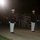 Marine Barracks Washington Evening Parade April 28, 2017 Two U.S. Marine Corps officers in dress blues (blue coat, white trousers, white covers) stand at attention during what appears to be an evening ceremonial parade or Evening Parade event. A crowd of spectators is seated on bleachers in the background. A red and gold Marine Corps flag is visible on the right side of the frame.