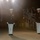 Marine Barracks Washington Evening Parade April 28, 2017 Two U.S. Marine Corps officers in dress blue uniforms stand at attention during a formal evening ceremony, likely a Friday Evening Parade or similar ceremonial event. They are positioned on a paved area illuminated by bright spotlights, with a crowd of spectators visible on bleachers in the background. The setting appears to be a military installation, possibly Marine Barracks Washington (8th & I).