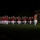 Marine Barracks Washington Evening Parade April 28, 2017 A military marching band performs an evening parade on a grass field, wearing distinctive red tunics and white trousers with white peaked caps. A drum major leads the formation at the front right, carrying a ceremonial mace. The event appears to take place at a military installation, with a brick building visible in the background.