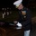 Marine Barracks Washington Evening Parade April 28, 2017 A senior U.S. Marine Corps officer in dress blues uniform is signing a document or program at a wooden podium during a nighttime military ceremony. Multiple Marines in dress uniforms are visible standing at attention in the background on a grass field. The setting appears to be a formal evening parade or ceremonial event at a military installation.