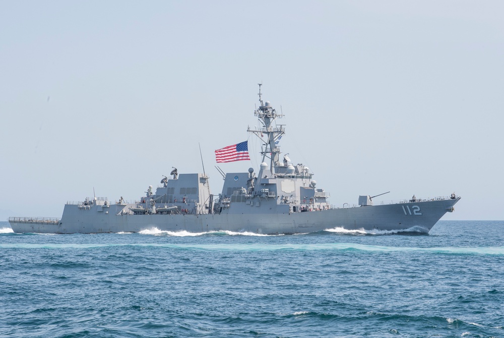 A United States Navy guided-missile destroyer bearing hull number 112 is underway at sea. The vessel is painted in standard naval gray and flies the American flag from its mast. The ship appears to be traveling at moderate speed, generating a visible wake.