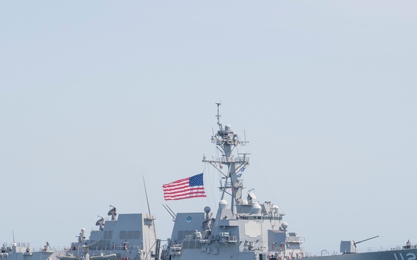 A United States Navy guided-missile destroyer bearing hull number 112 is underway at sea. The vessel is painted in standard naval gray and flies the American flag from its mast. The ship appears to be traveling at moderate speed, generating a visible wake.