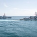 Two U.S. Navy guided-missile destroyers are underway in open ocean, sailing in close formation. Both vessels are flying American flags and appear to be Arleigh Burke-class destroyers based on their hull design and superstructure configuration. The ships are creating visible wakes as they navigate through calm to moderately choppy blue-green waters.