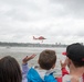 Crowd waves as an HH-65 Dolphin helicopter hoists a rescue swimmer during a search and rescue demonstration