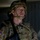 A U.S. Army soldier in full combat gear is photographed in a low-light indoor environment, likely during a training exercise or operational deployment. The soldier is wearing MultiCam (OCP) pattern uniform and body armor, with a combat helmet secured by a chin strap. The image has a serious, documentary-style composition with dramatic lighting.