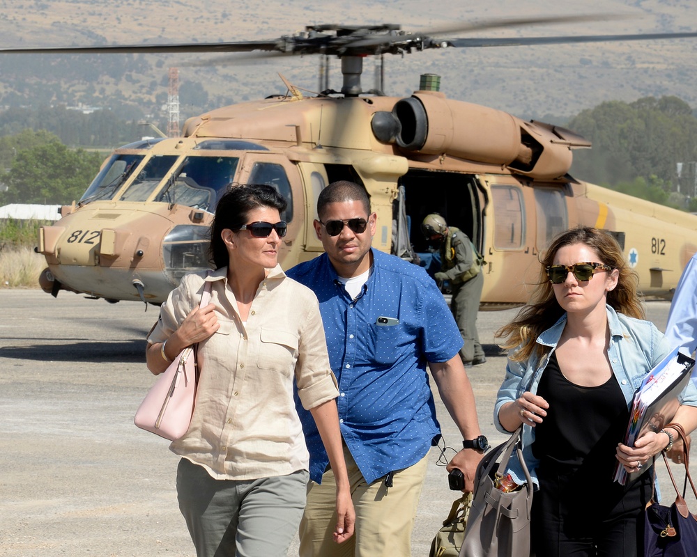 Three civilians walk away from a military helicopter on a tarmac or airfield. The helicopter, numbered '812' and painted in tan/desert camouflage, appears to be a Sikorsky UH-60 Black Hawk variant with a Star of David marking visible, suggesting Israeli military affiliation. A flight crew member in a green flight suit can be seen near the aircraft in the background.