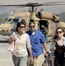 Three civilians walk away from a military helicopter on a tarmac or airfield. The helicopter, numbered '812' and painted in tan/desert camouflage, appears to be a Sikorsky UH-60 Black Hawk variant with a Star of David marking visible, suggesting Israeli military affiliation. A flight crew member in a green flight suit can be seen near the aircraft in the background.