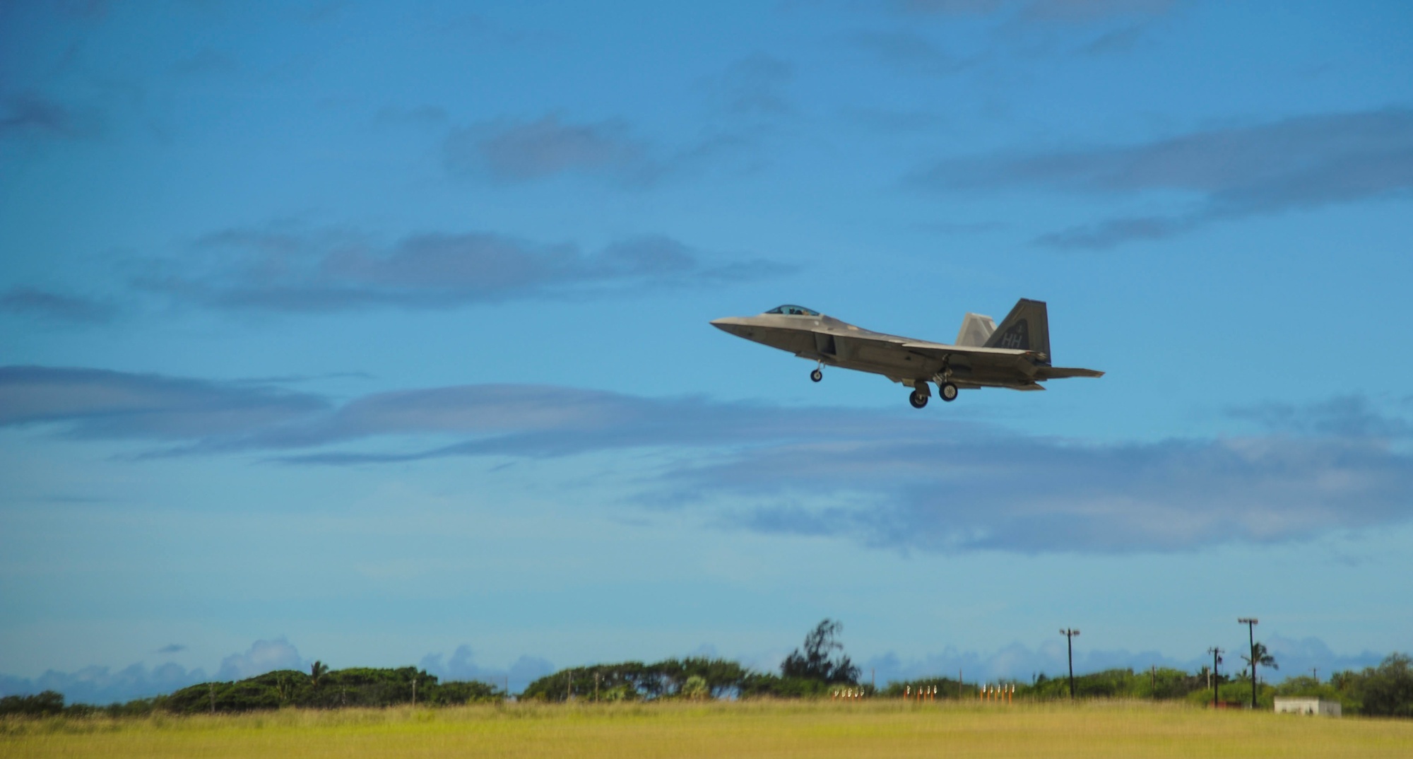 Side view of a gray F-22 approaching a runway with landing gear extended, showing its pointed nose, canopy, and twin tails.