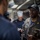 170612-N-MJ135-128 The image shows what appears to be a U.S. Navy inspection or briefing taking place in a shipboard galley (kitchen). Several personnel in Navy uniforms are present, including one individual in a gray coverall uniform with officer insignia who appears to be speaking or conducting an inspection. A cook in a white chef's hat is visible in the background taking notes.