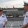 Sterett-Dewey Surface Action Group Deployment Two naval officers, one wearing a U.S. Navy uniform and one wearing a People's Liberation Army Navy (PLAN) uniform, are engaged in conversation on the deck of a naval vessel. Both the American flag and Chinese flag are visible in the background, suggesting a bilateral military exchange or port visit. The setting appears to be a naval base or harbor.