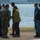 170615-N-SD711-0055 A group of military personnel and civilians are gathered near a waterfront, appearing to engage in a greeting or reception ceremony. Multiple uniform types are visible, including U.S. Navy blue digital camouflage (NWU Type I) and what appears to be a light blue digital camouflage uniform worn by a foreign military member. A handshake is visibly occurring between individuals in the center of the group.