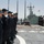 170614-N-FQ994-134 A group of U.S. Navy personnel in dark blue coveralls and ball caps are standing in formation on the deck of a naval vessel, likely during a port call or muster. A second warship, possibly a Canadian or allied naval vessel, is visible moored alongside in the background. The scene appears to take place in a harbor or naval base under clear, sunny conditions.