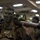 170614-N-GG458-053 A U.S. Marine with green and black camouflage face paint carries a shoulder-fired rocket launcher (appears to be an M3 MAAWS or similar recoilless weapon system) on his shoulder inside what appears to be a ship's well deck or hangar bay. He is wearing MARPAT digital camouflage utilities and tactical gear with visible name tape and unit markings. Additional Marines with similar gear and face paint are visible in the background.