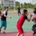 Sterett-Dewey Surface Action Group Deployment A basketball game is being played on an outdoor court, likely at a Chinese university or sports facility. Multiple players in red uniforms are competing against players in gray and dark jerseys, with one player holding the ball while being defended. The setting includes multiple basketball courts, surrounding greenery, and institutional buildings in the background.