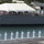 170613-N-HX806-058 A formal naval ceremony is taking place at a harbor, with a line of sailors in white dress uniforms standing at attention on a dock facing a large warship bearing the hull number 63. The ship, identifiable as USS Missouri (BB-63) or a vessel with that hull number, has large naval gun turrets visible and a crowd of civilians gathered on its deck under a white event tent. The setting appears to be Pearl Harbor, Hawaii, based on the tropical vegetation and recognizable maritime infrastructure.